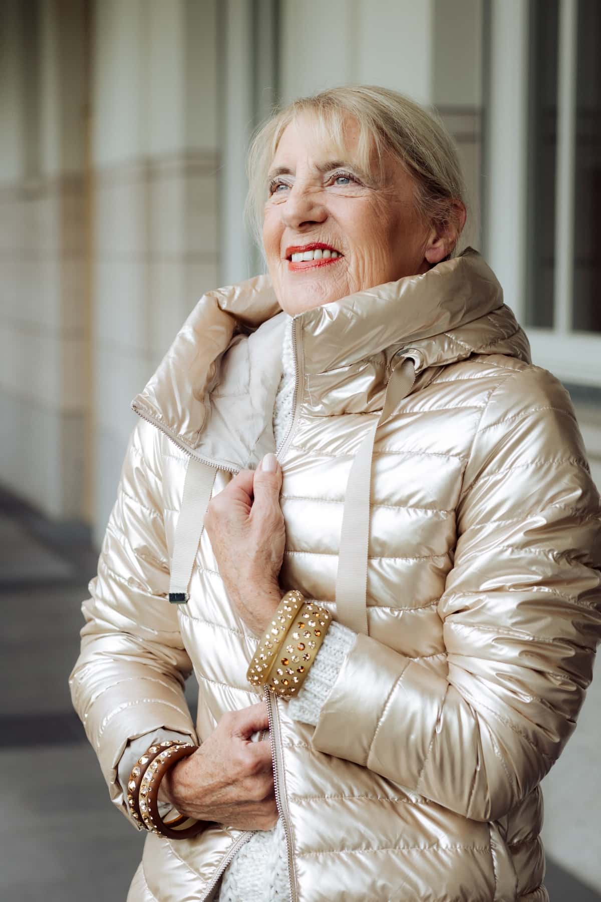 Bestager Frau in goldener Winterjacke mit beigen Coloristers Armreifen mit Kristallen. Bestager women wearing golden winter jacket with beige Coloristers bangles with crystals.
