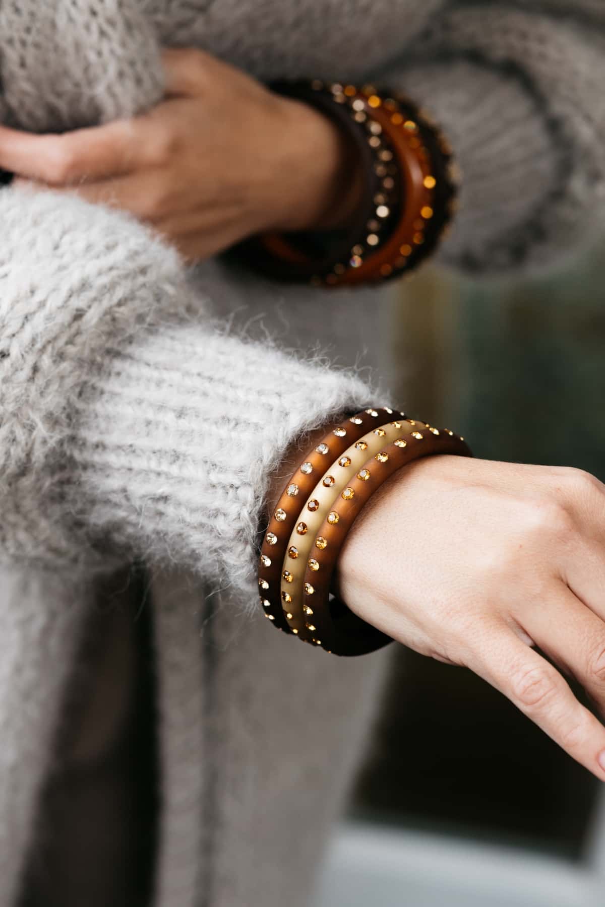 Hand mit beigen und braunen Armreifen mit Kristallen. Hand with brown and beige bangles with crystals.