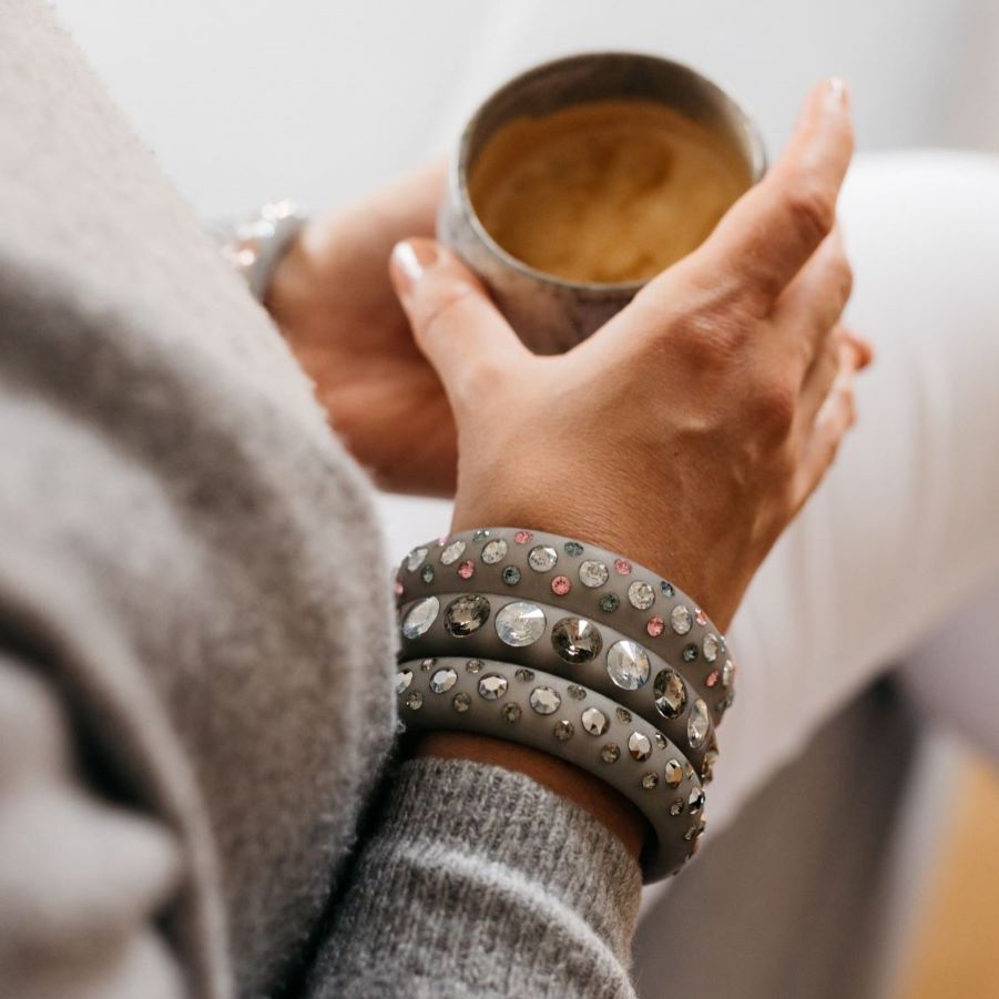 Hand mit grauen Armreifen mit Kristallen hält eine tasse kaffee. Hand with grey bangles with crystals holds cup of coffee..
