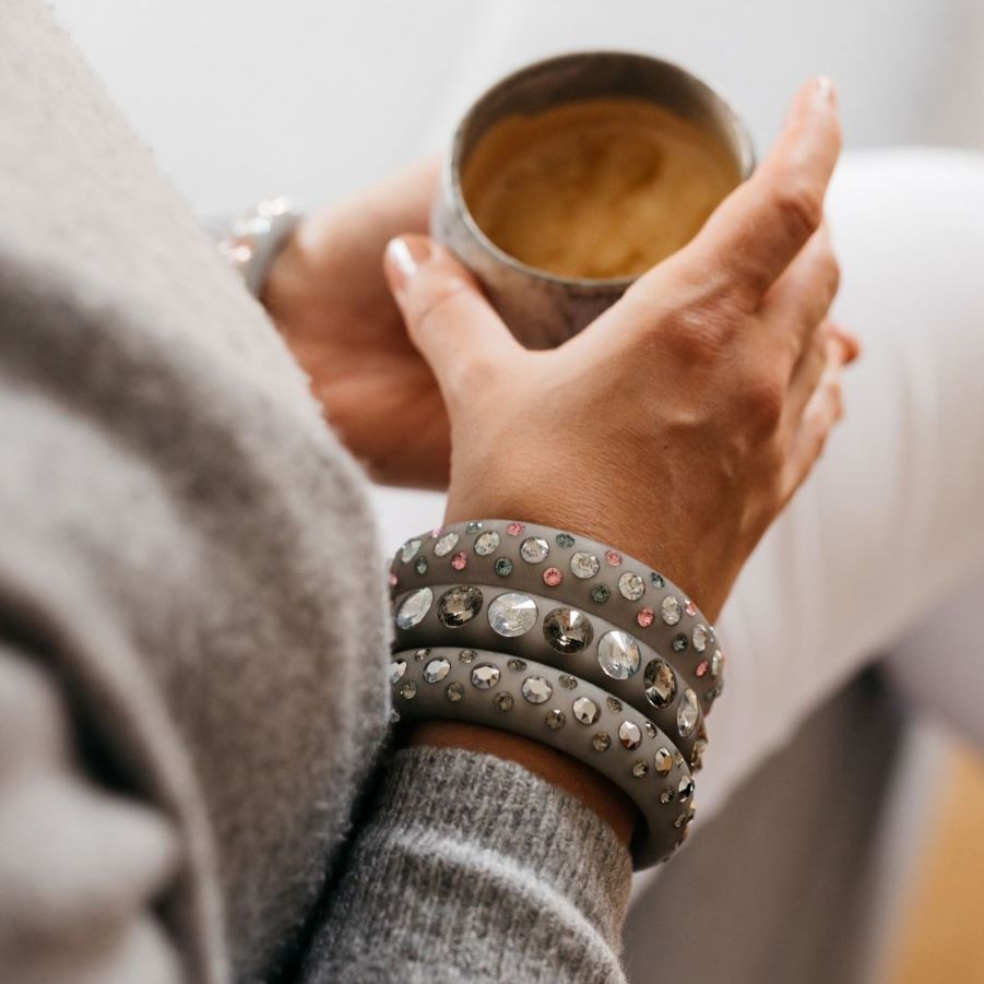 Hand mit grauen Armreifen mit Kristallen hält eine tasse kaffee. Hand with grey bangles with crystals holds cup of coffee.. 