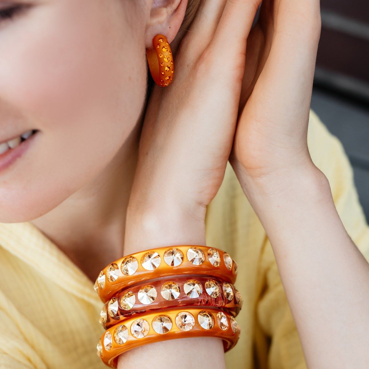 Frau mit orangenen Ohrringen und Armreifen mit Kristallen. Woman with orange earrings and bangles with crystals.