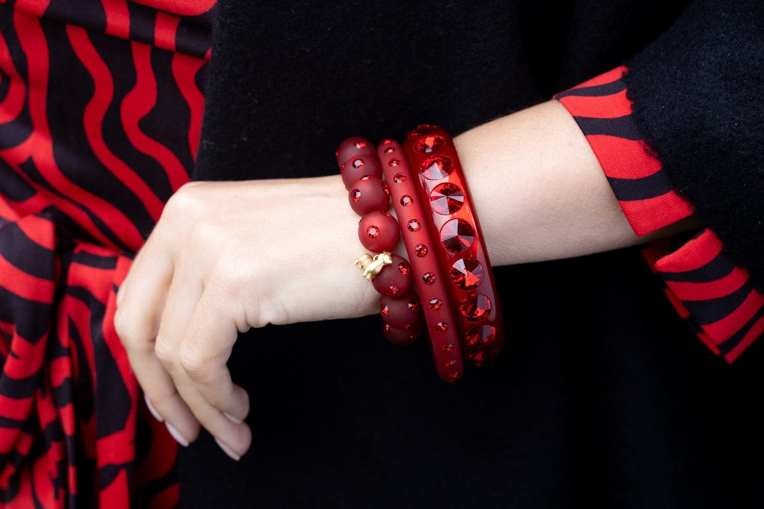 Hand mit Coloristers Armreifen in dunkel rot mit Kristallen. Hand with Coloristers bangles in dark red with crystals.