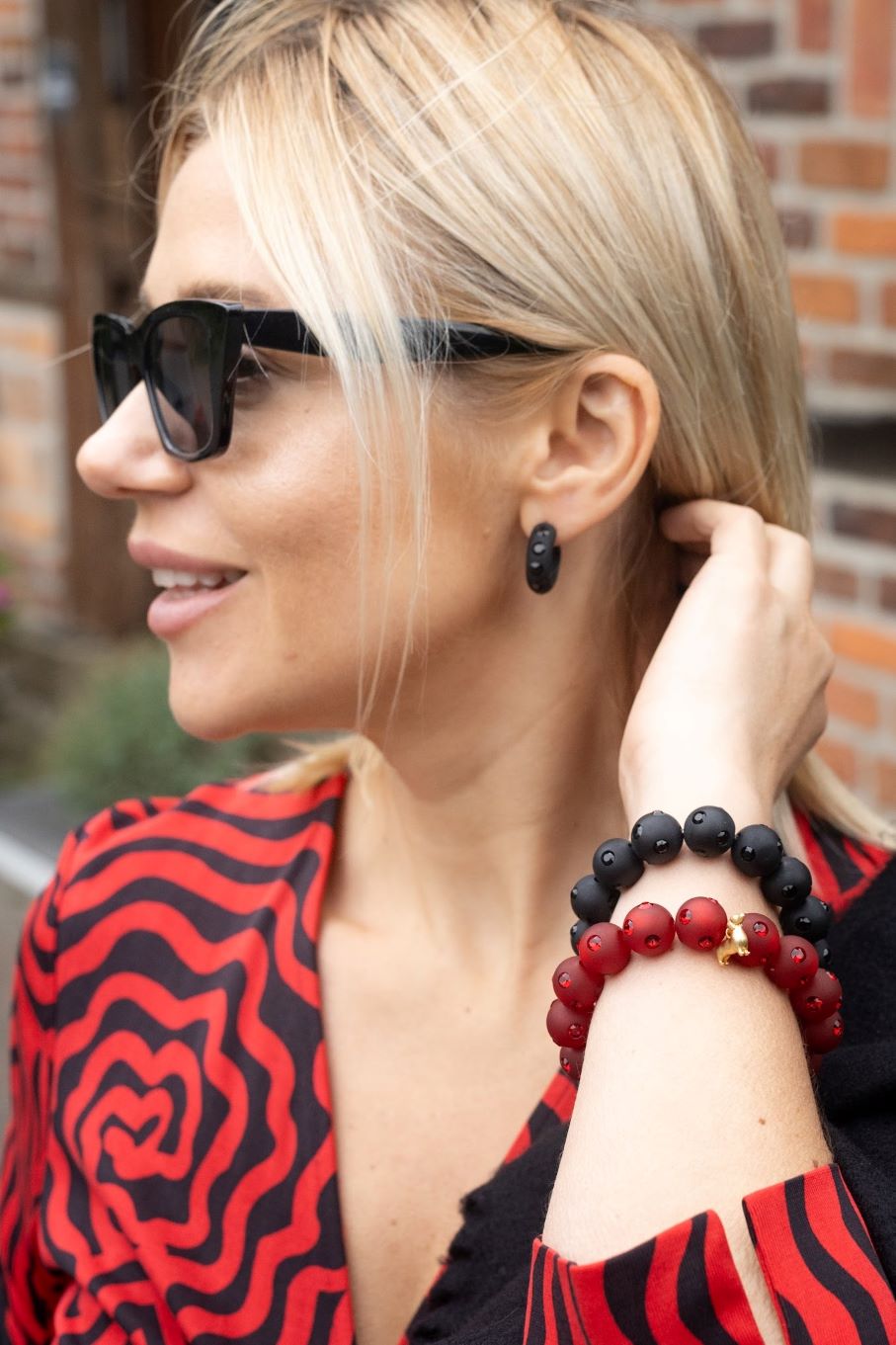 Frau mit Coloristers Ohrringen und Perlenarmband in dunklem rot mit Kristallen. Women with Coloristers earrings and pearl bracelet in dark red with crystals.