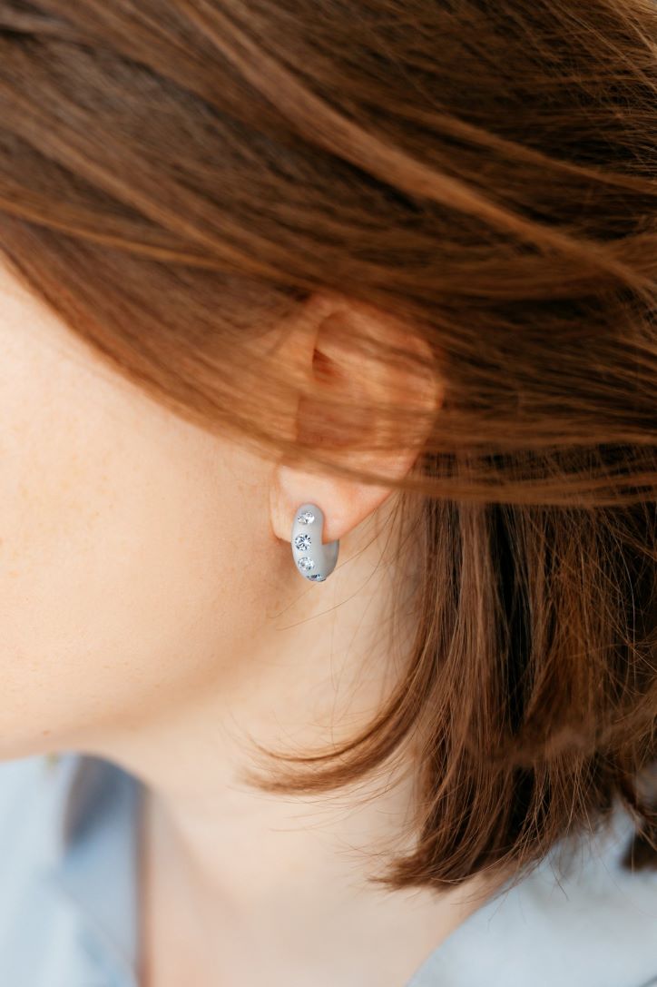 Frau mit Kleinen Coloristers Creolen mit Kristallen in grau. Woman with small Coloristers creole earrings with crystals in grey.