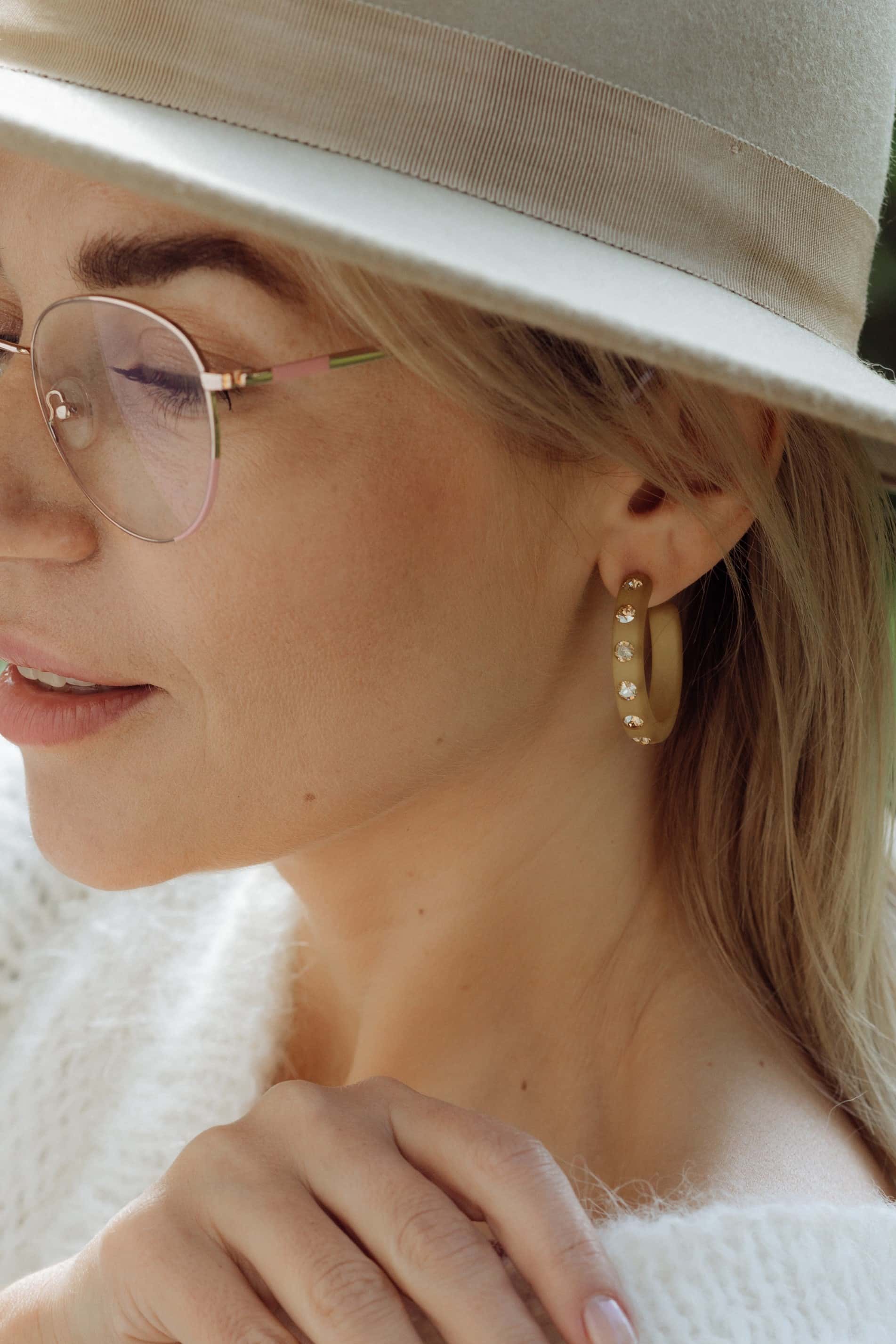Frau mit Coloristers Ohrringen Creolen mit Kristallen in Beige. Woman with Coloristers earrings creoles with crystals in beige.